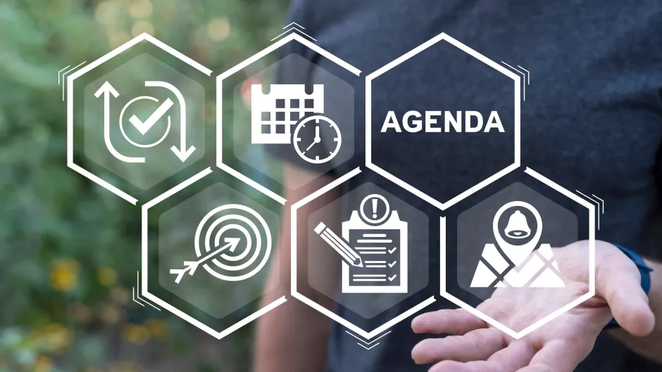 Blick auf Grafik in Bienenwabenform mit fünf Symbolen und einer Wabe, die mit "Agenda" beschriftet ist - im Hintergrund balanciert ein verschwommener Mensch das Gebilde in der offenen Hand